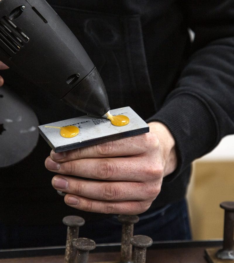 Man applying small beads of hot melt adhesive to a steel insert