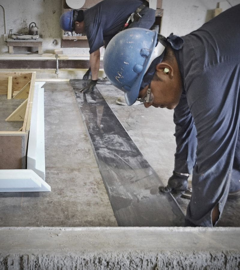 Men applying a thin plastic piece to the bottom of a concrete precast mould