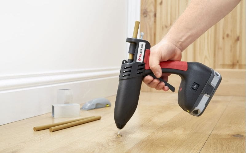 Man applying Knottec hot melt filling compound to a knot in hardwood floor
