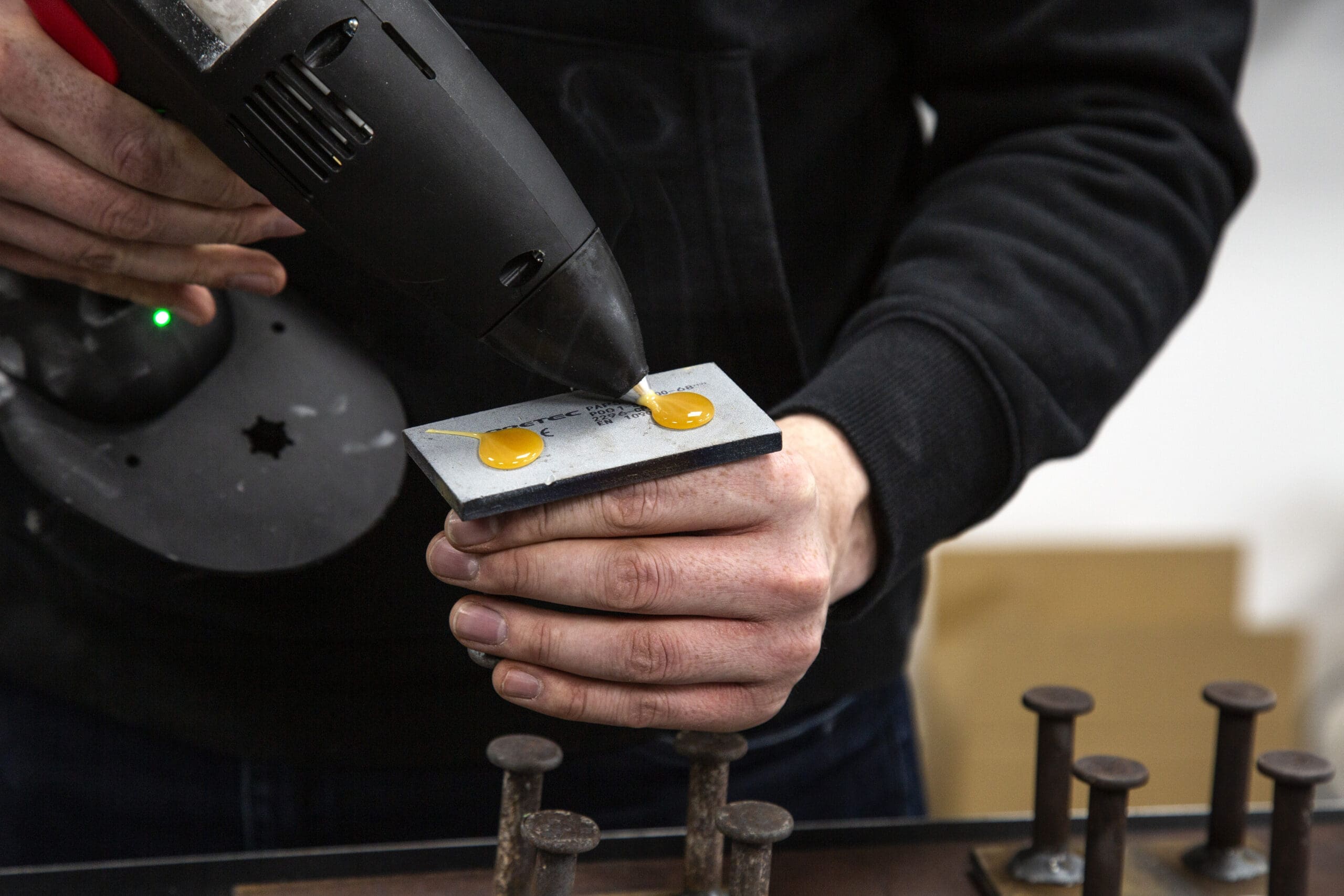 Man applying small beads of hot melt adhesive to a steel insert